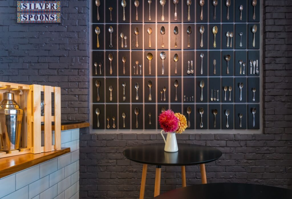 Interior of contemporary cafeteria with various silver spoons on brick wall near bar counter and round table