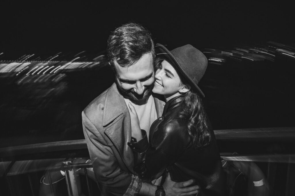 A couple shares a joyful embrace at night in a black and white photo.