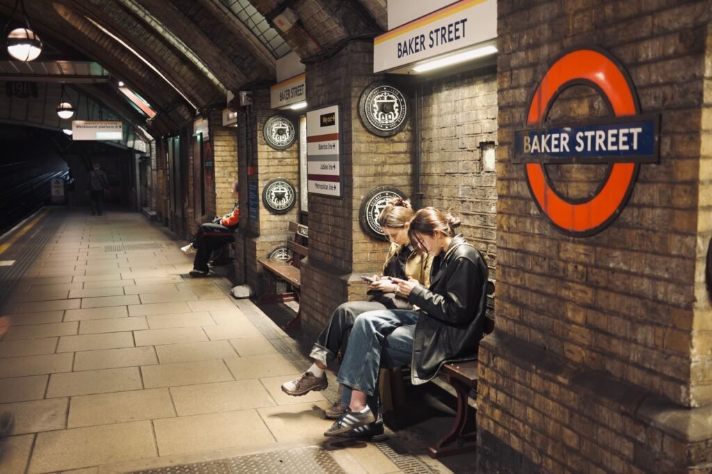 Two people seated using phones at Baker Street London station.