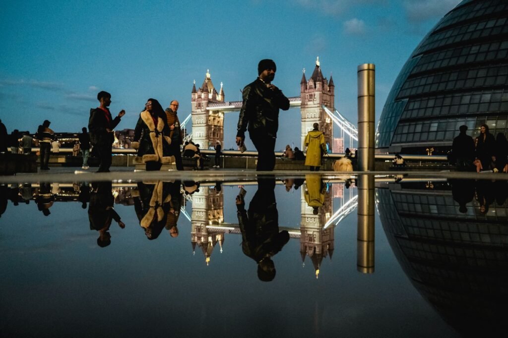 Silhouettes of people reflected in a puddle with Tower Bridge in the background, London.