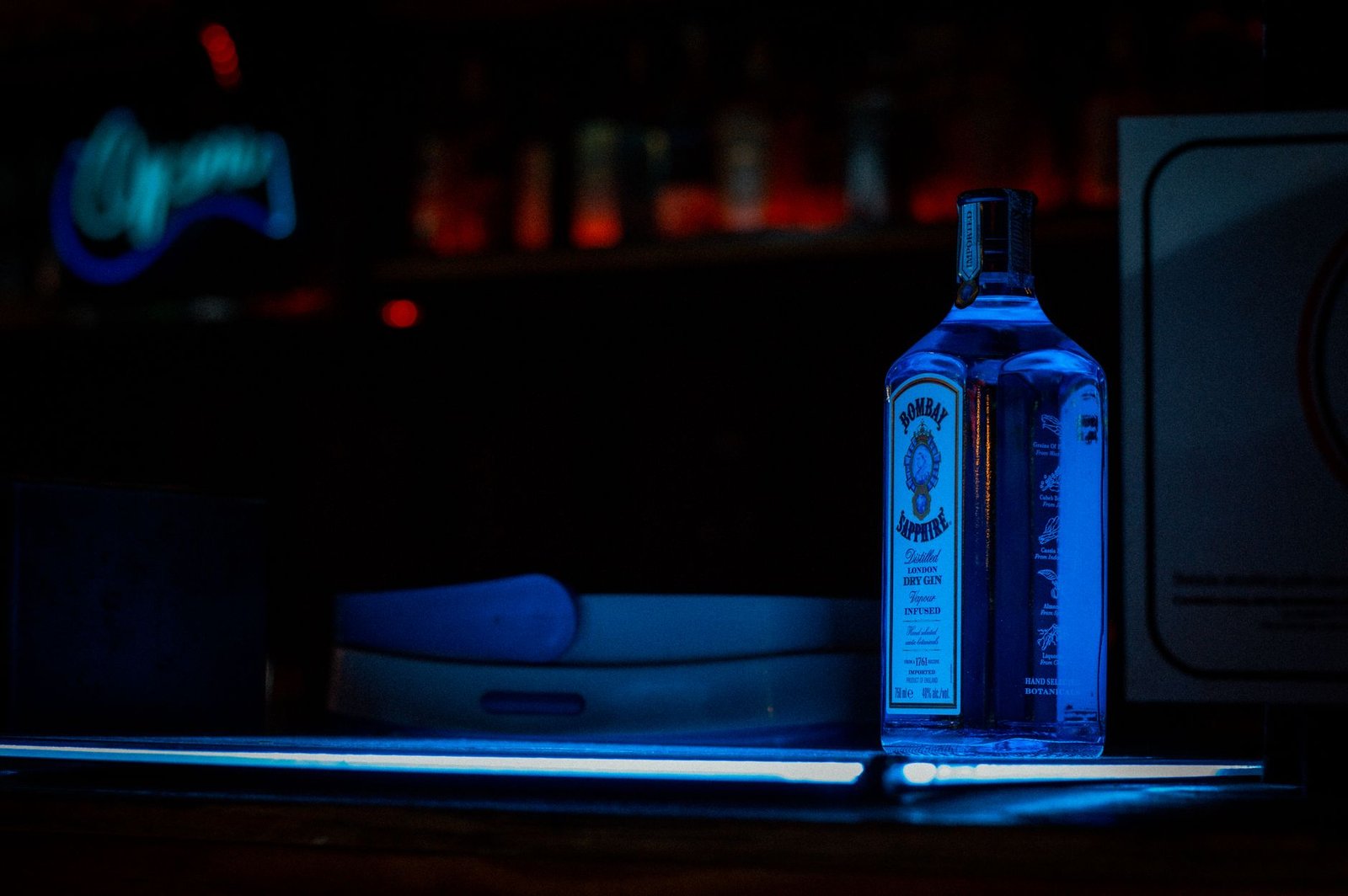 Bombay Sapphire gin bottle illuminated under blue light at a bar, creating an atmospheric nightlife vibe.