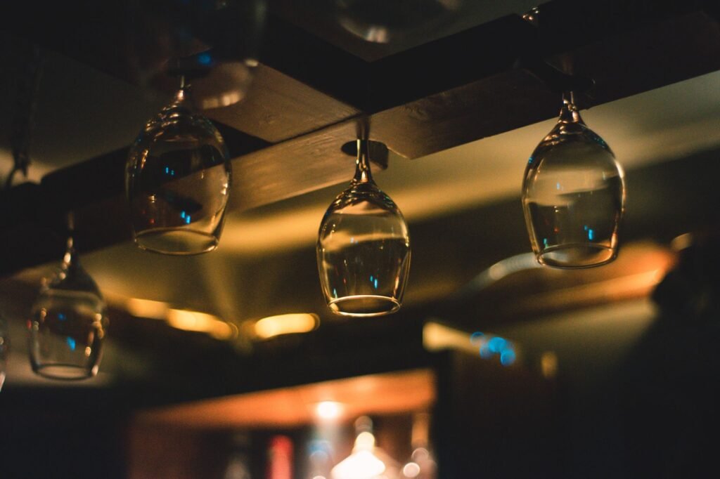 Close-up of hanging wine glasses with bokeh lights in a dimly lit bar setting, creating a soft, warm ambiance.