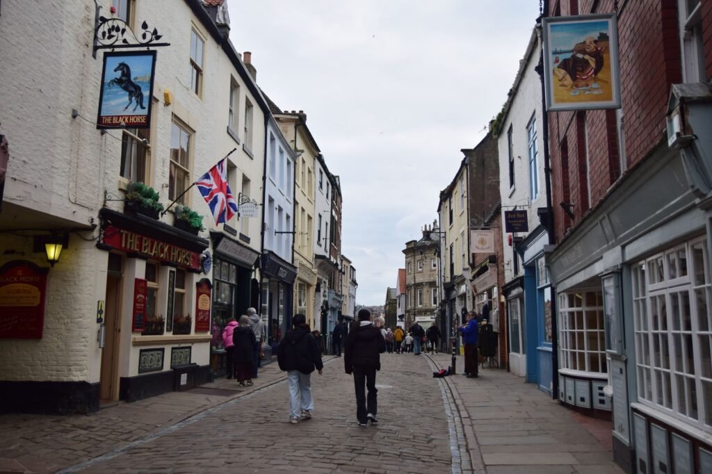 Cobblestone street lined with quaint shops and Union Jack flag in a historic English town.