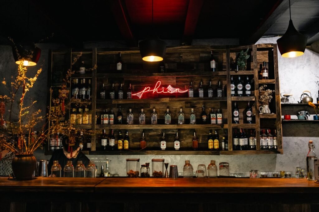 Cozy bar interior with wooden shelves, bottles, and a red neon sign creating a warm ambiance.