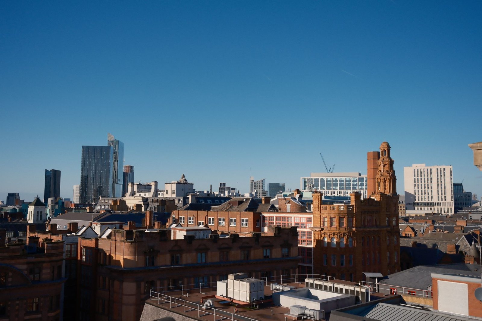 Aerial view of Manchester city skyline featuring modern and historic architecture under a clear blue sky.