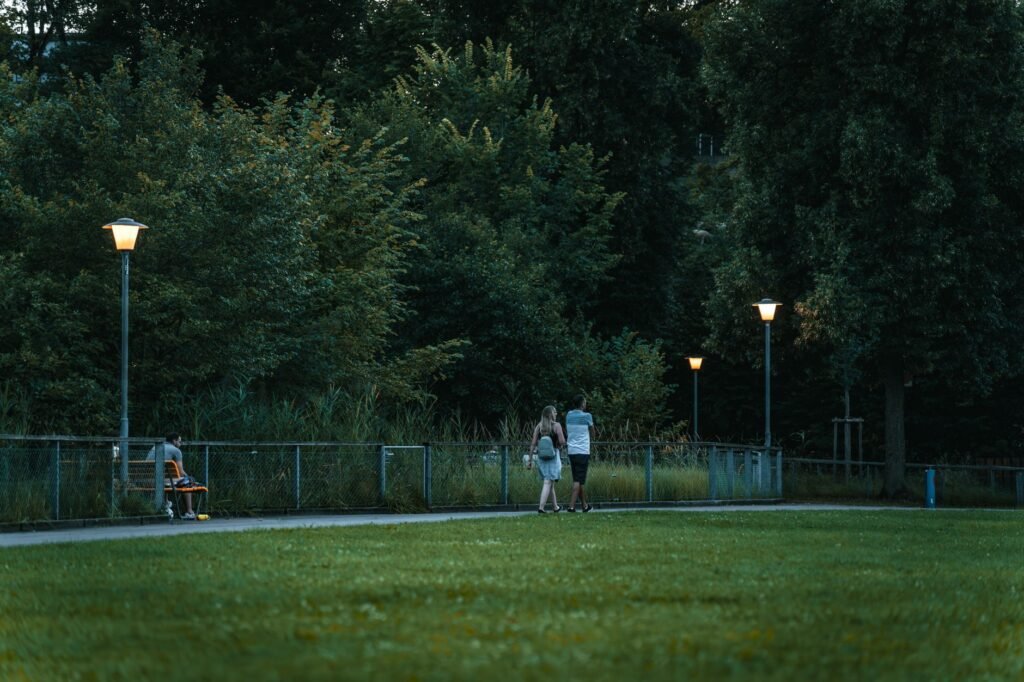 Couple strolling along a path in a serene park at dusk with street lights lit softly.