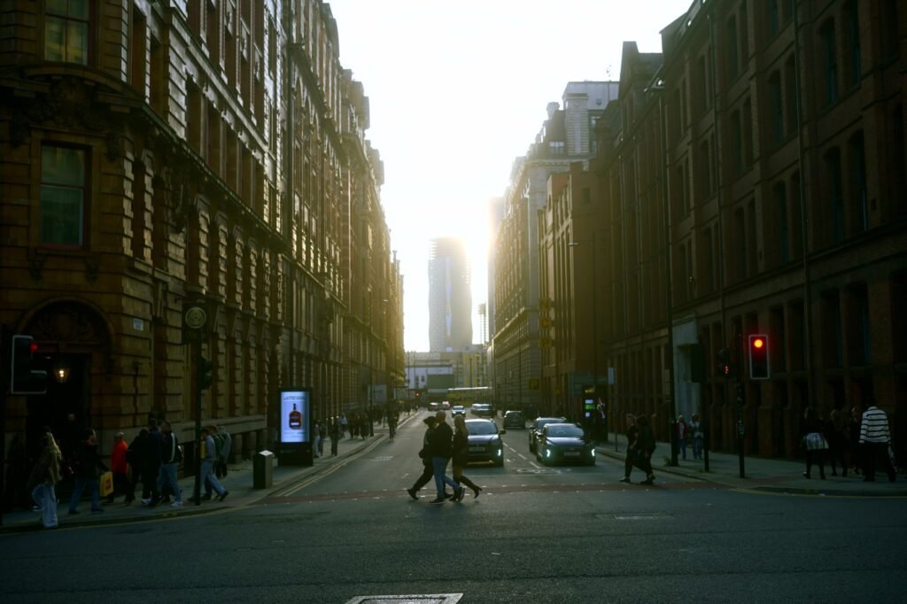 City street at sunset with people crossing, cars, and tall buildings.