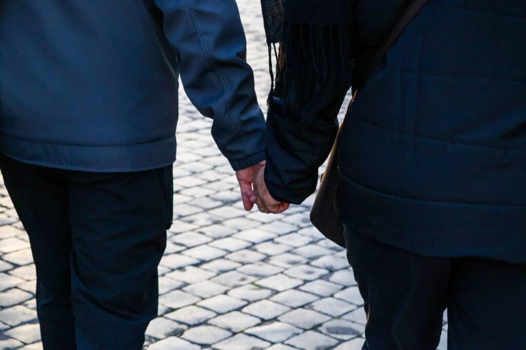 Back view of a couple holding hands walking on a cobblestone street.