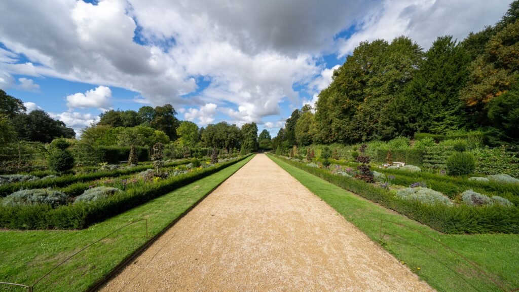 Explore the serene landscape of Dyrham Park gardens in England, featuring lush greenery and a tranquil pathway.