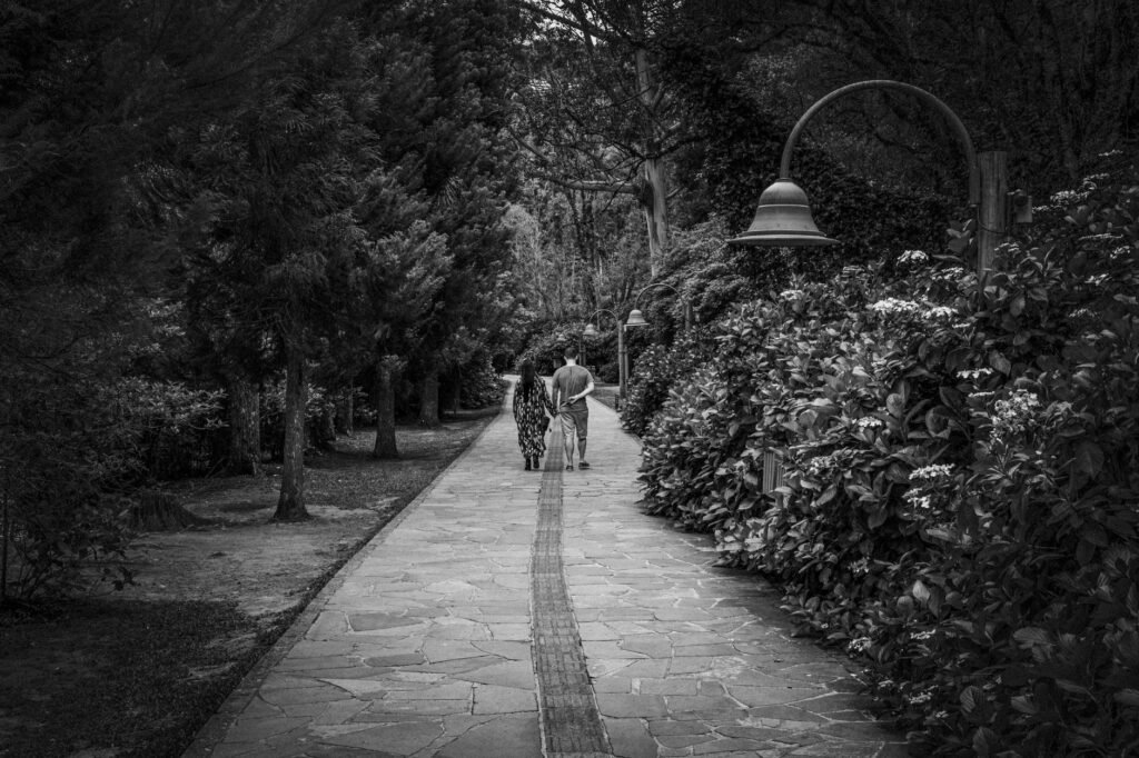 A couple strolls through a serene park pathway, captured in timeless black and white.