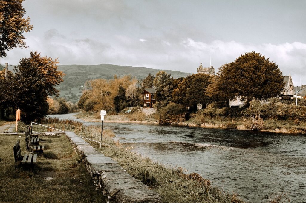 Serene riverside landscape in Llanrwst, Wales, featuring benches and natural scenery.