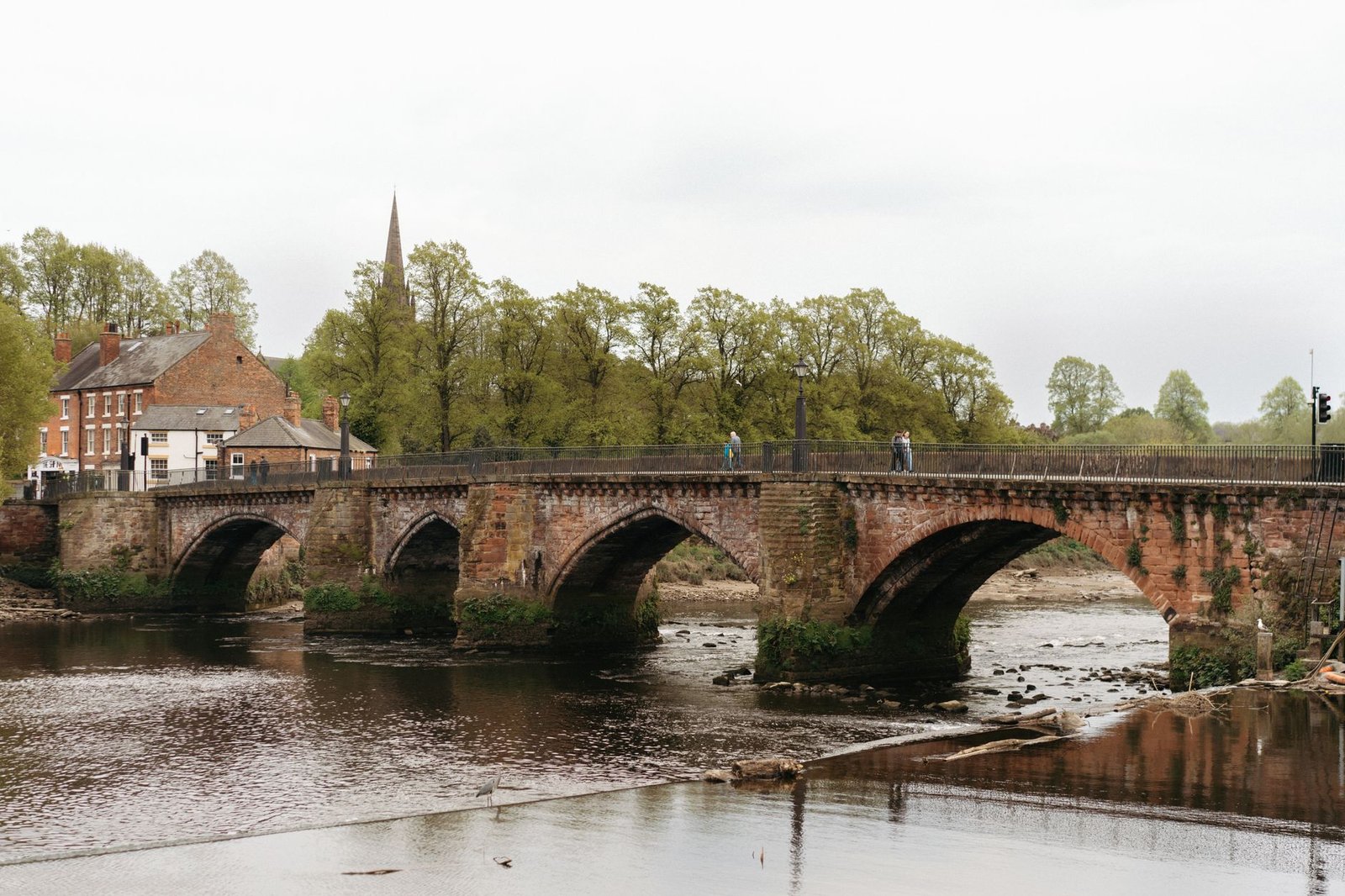Historic stone bridge over River Dee in Chester, UK with lush greenery.