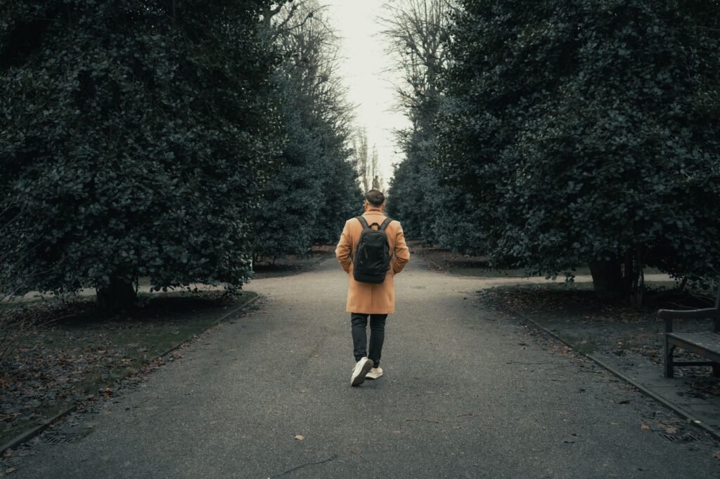 A man in a coat and backpack walks a path in Chester's autumn park.