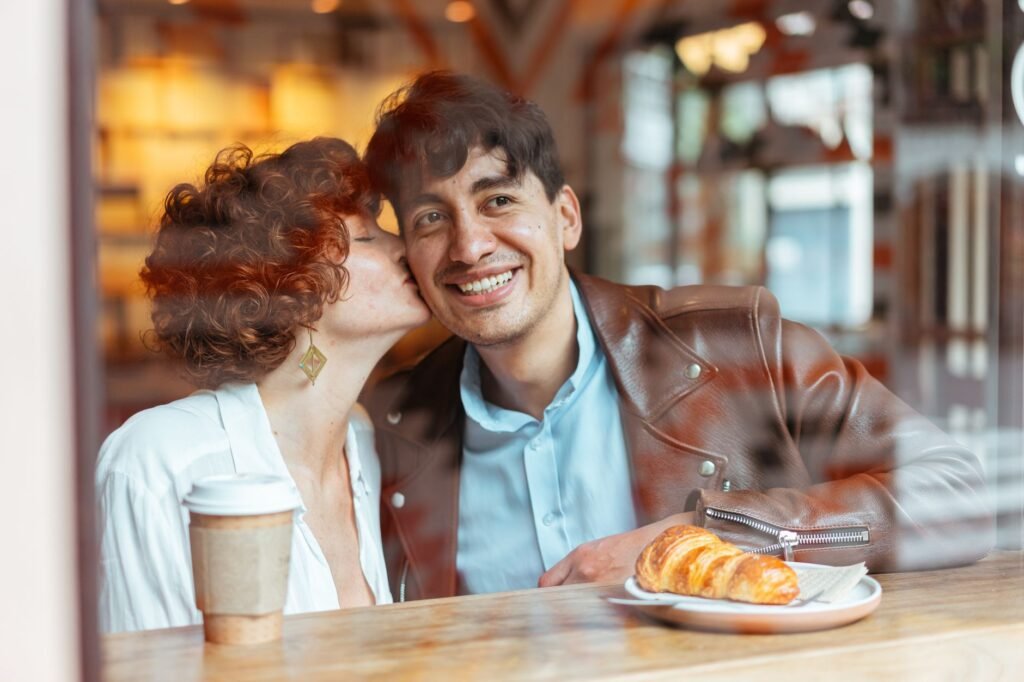 A joyful couple sharing a sweet moment in a cozy café setting, enjoying a croissant and coffee.