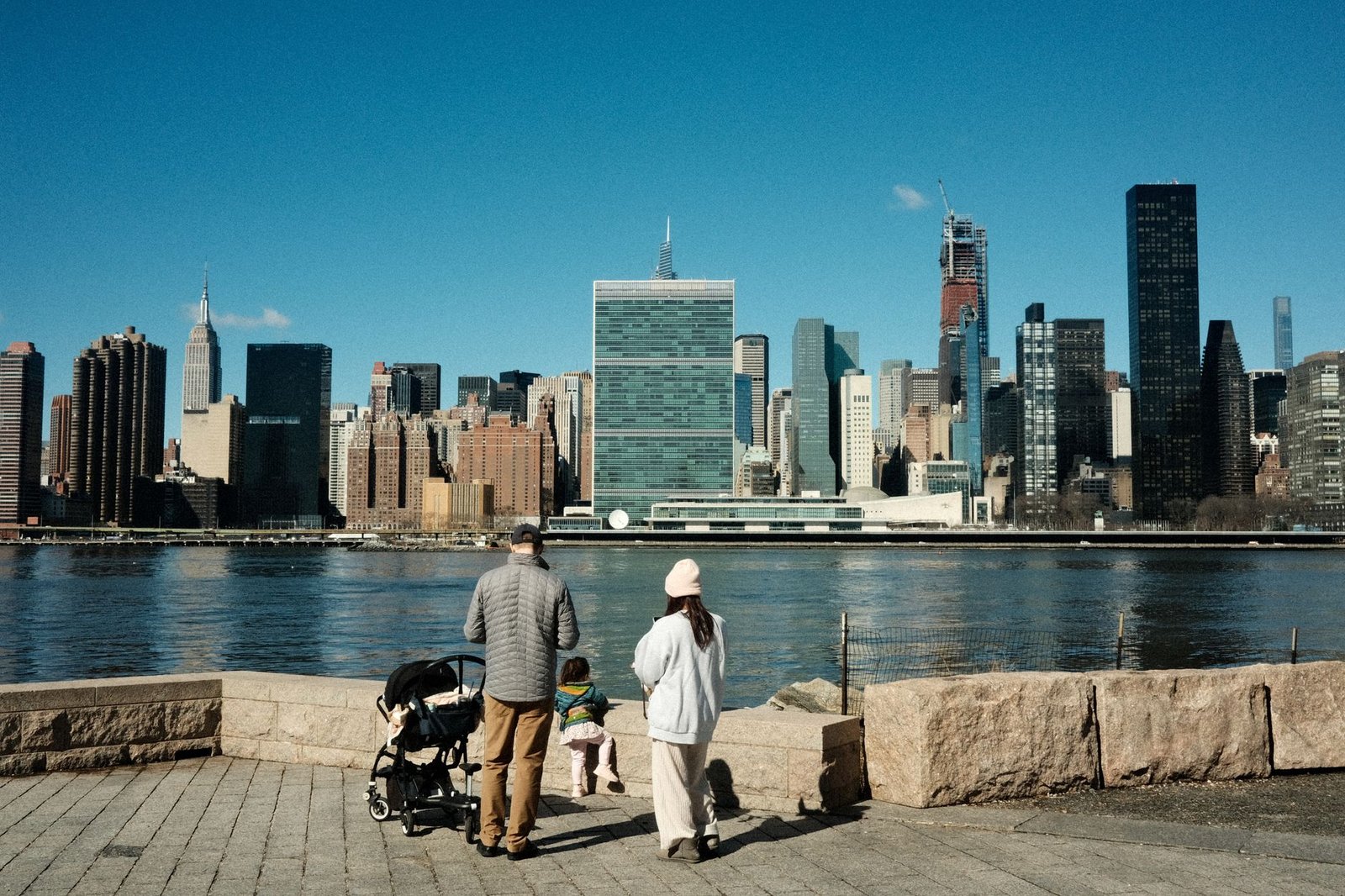 A family enjoys a riverside stroll with New York City's iconic skyline as the backdrop.