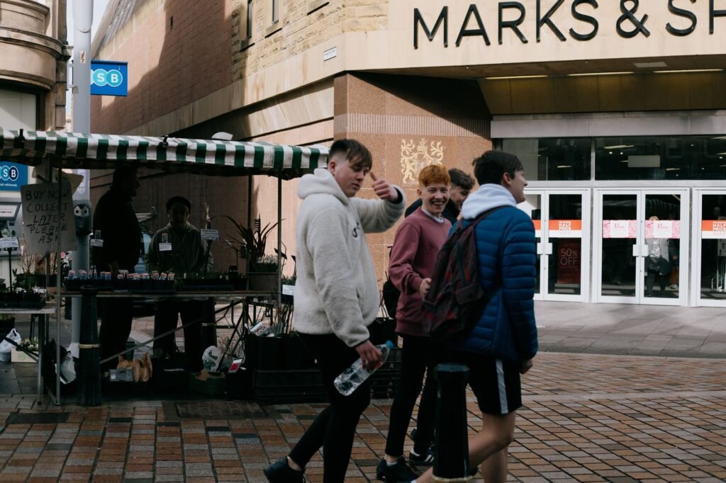 Side view content teenage boy in warm sweater strolling on city street with fellows and showing thumb up to camera