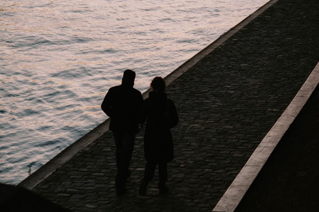 A couple walks along a riverside path at dusk, capturing a peaceful and romantic moment.