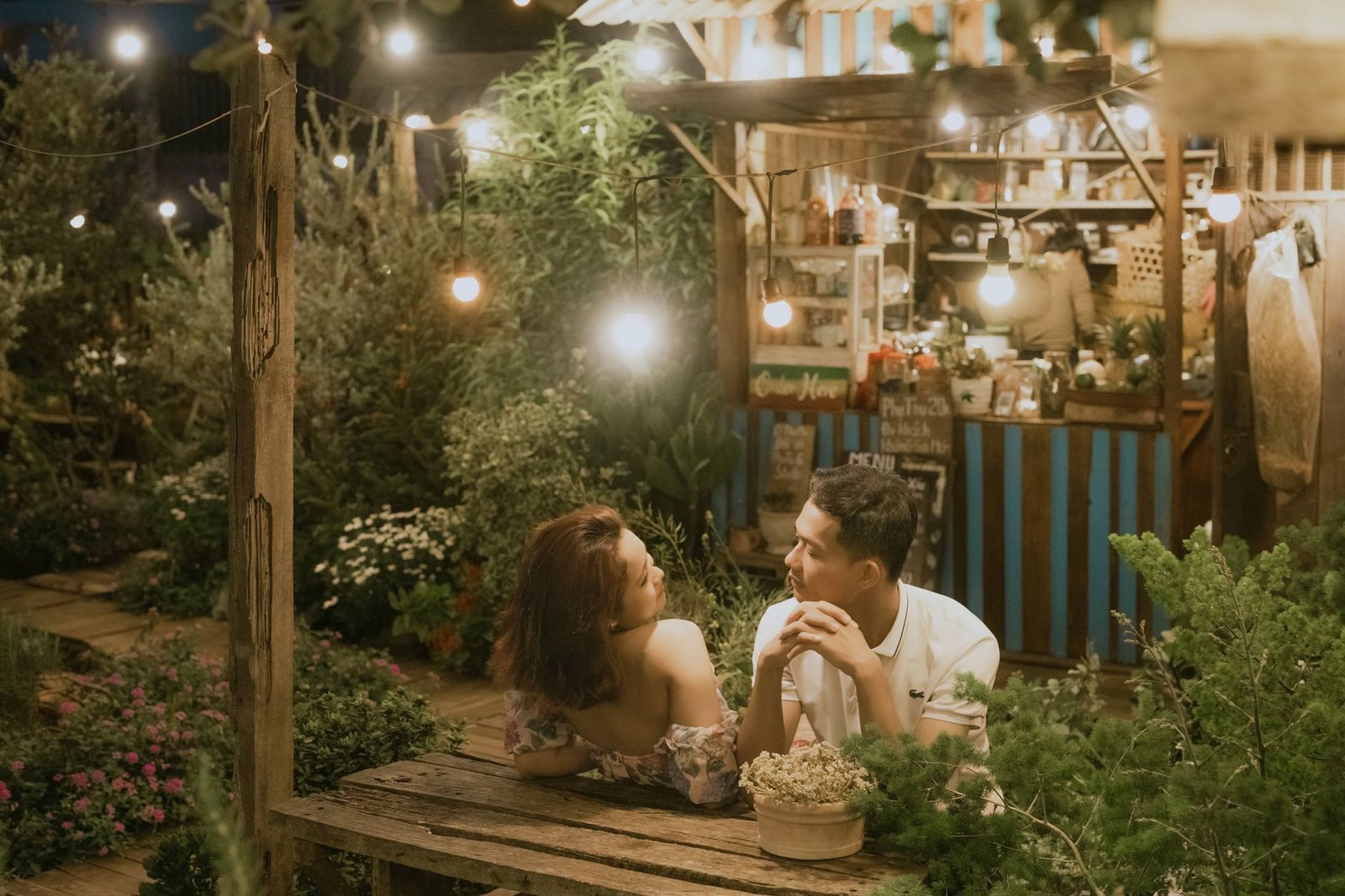 Couple enjoying a romantic evening at an illuminated garden café under string lights.