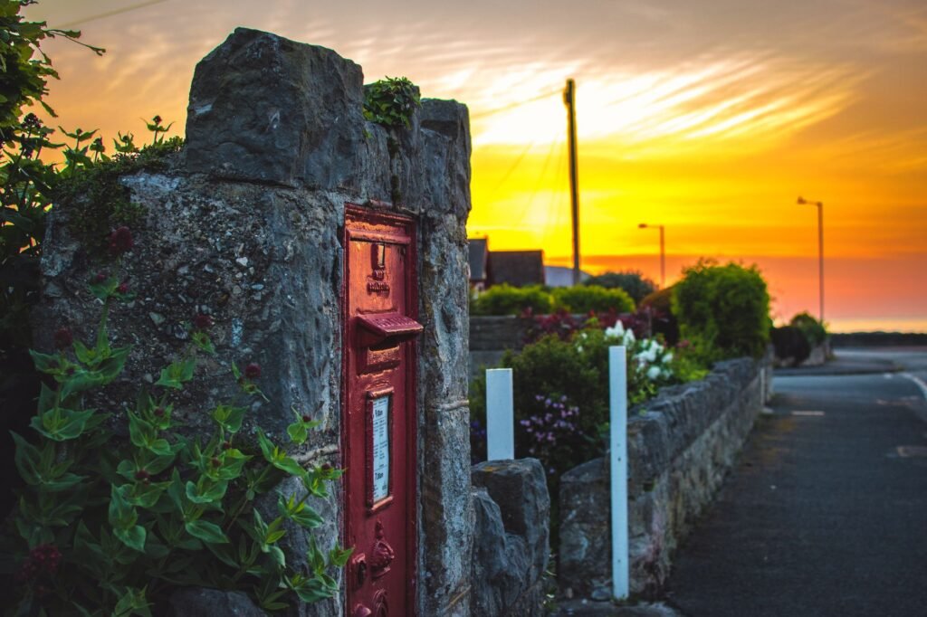 An old red postbox on a stone wall with sunset in a picturesque village street