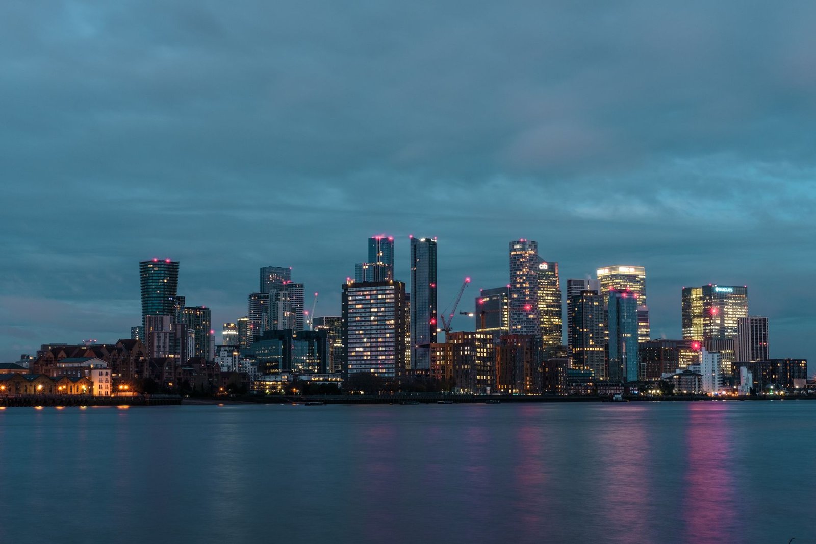 Evening view of the illuminated skyline of Canary Wharf, reflected on water, United Kingdom.