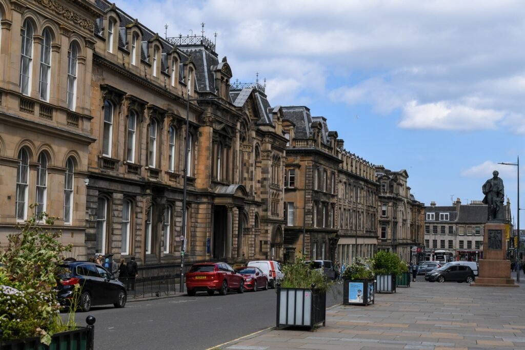Street view of historical architecture in Edinburgh, Scotland, featuring classic stone buildings and a statue.