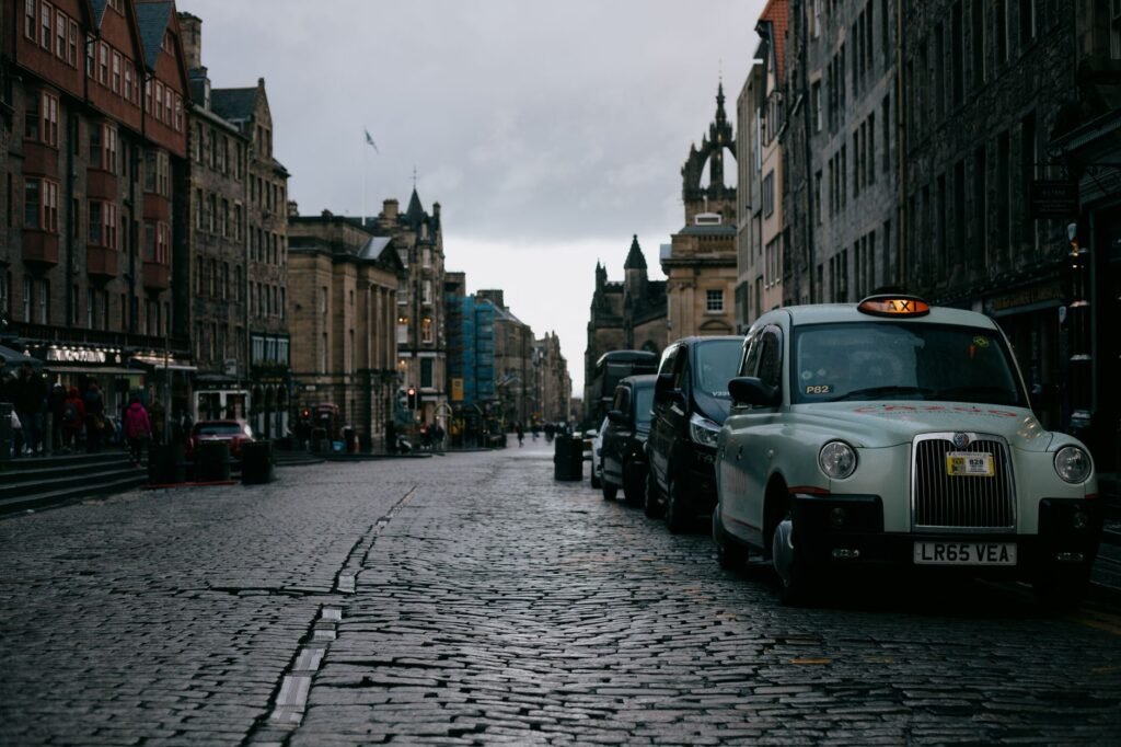 Street with parked cars between aged multistage building exteriors under gray sky in city