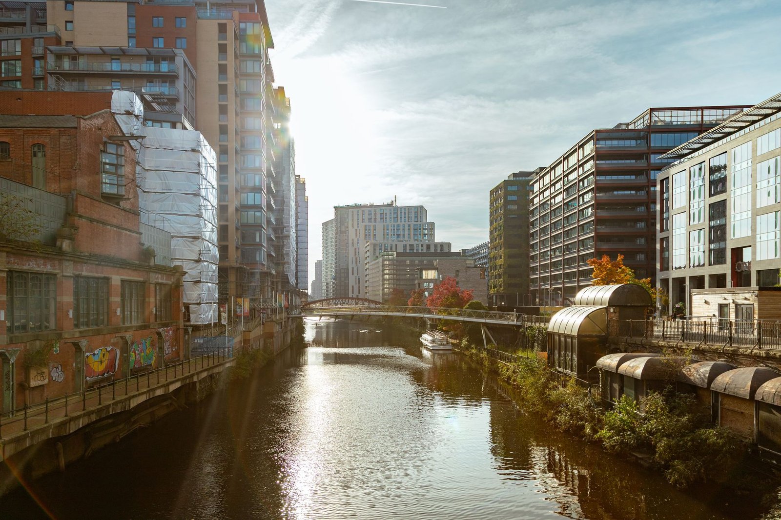 A vibrant cityscape of Manchester with modern and historic buildings by a canal.