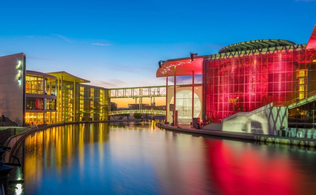 Stunning view of illuminated modern buildings by the river at sunset with vibrant reflections.