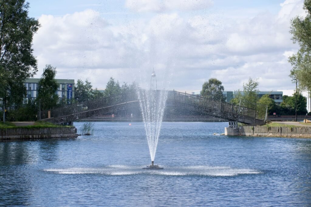 A picturesque fountain amidst a tranquil city park with a bridge and natural scenery.