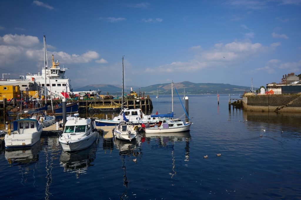 A tranquil scene of boats docked at Rothesay Harbor, Isle of Bute, Scotland, under a clear summer sky.