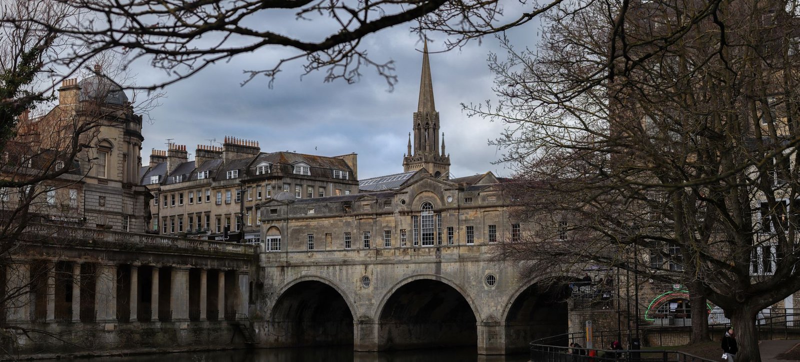 A classic view of Pulteney Bridge in Bath, England with winter trees framing the historic architecture.