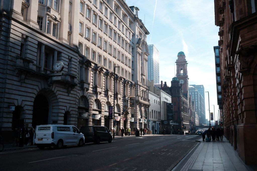 A bustling street in Manchester showcasing historic architecture and urban life on a sunny day.