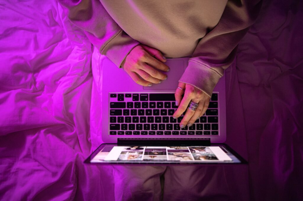 Top view of unrecognizable person using laptop with neon purple lighting, creating a vibrant high-tech atmosphere.