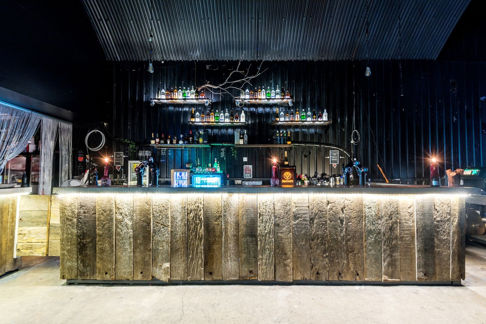 A stylish and modern bar interior featuring a rustic wooden counter and ambient lighting, creating a unique nightlife atmosph