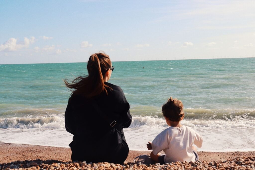 A serene moment between mother and child on the pebbly beach of Brighton, UK, on a sunny day.