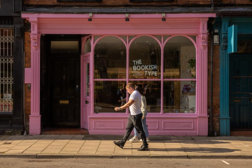 Vibrant pink bookstore facade on a sunny street in Leeds, UK, with people walking by.