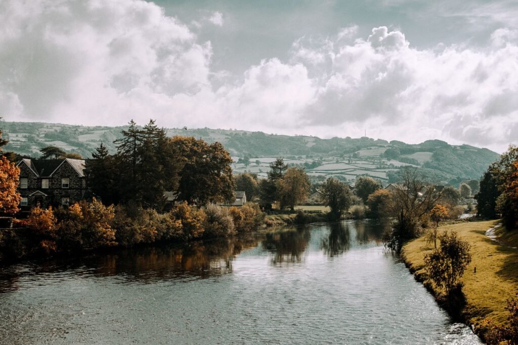 Picturesque autumn view of a river in Llanrwst, Wales with lush greenery and dramatic clouds.
