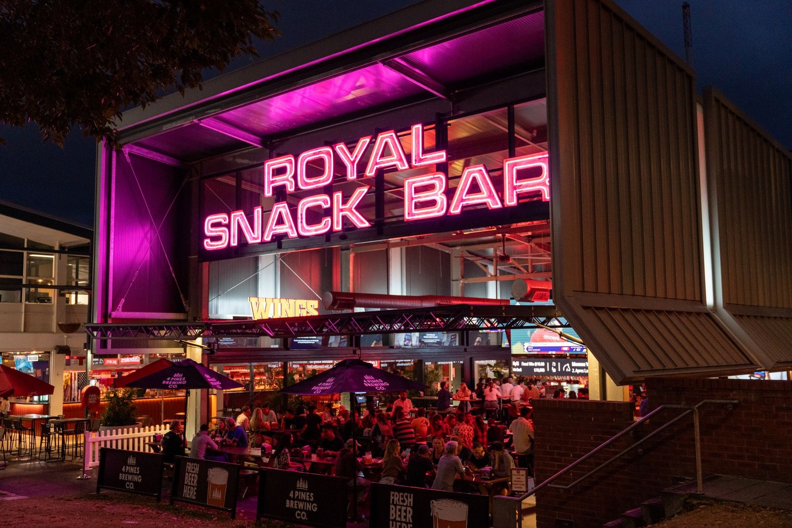 Visitors enjoy a lively night at Royal Snack Bar in Bowen Hills with vivid pink neon lights.