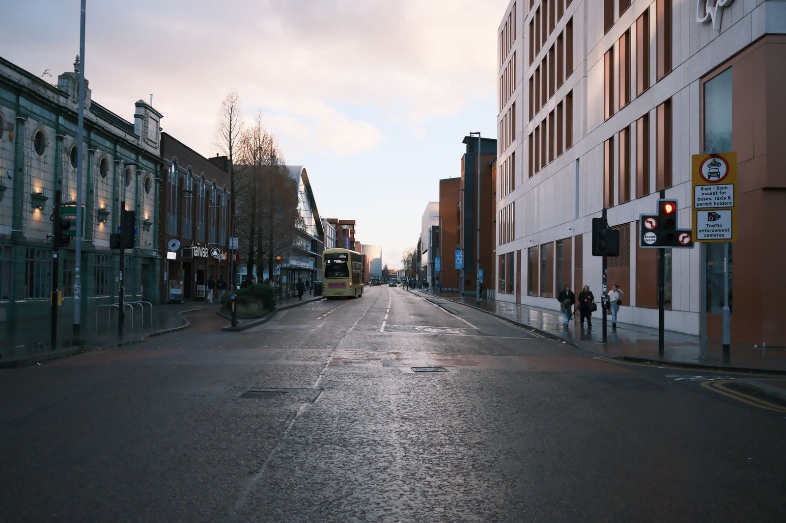 A quiet urban street highlighting a double decker bus and modern architecture under a cloudy sky.