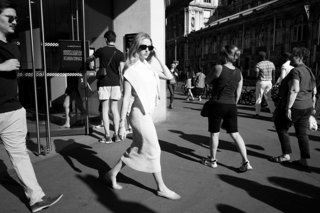 Black and white photo of a stylish woman walking confidently in a bustling urban street.