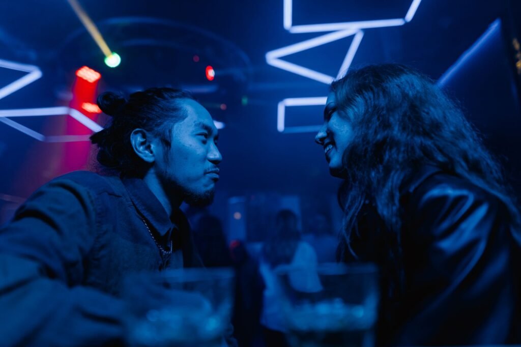 A couple enjoys a night out, conversing under vibrant neon lights in a stylish bar.