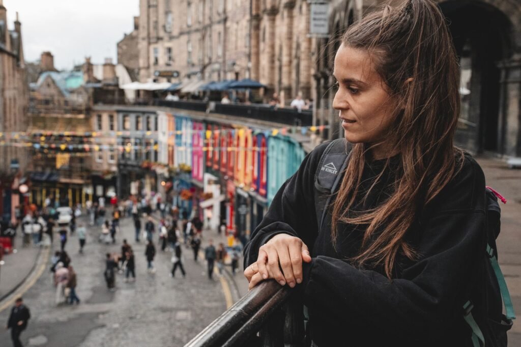 A young woman leans on a railing, overlooking a vibrant street in Edinburgh, Scotland.