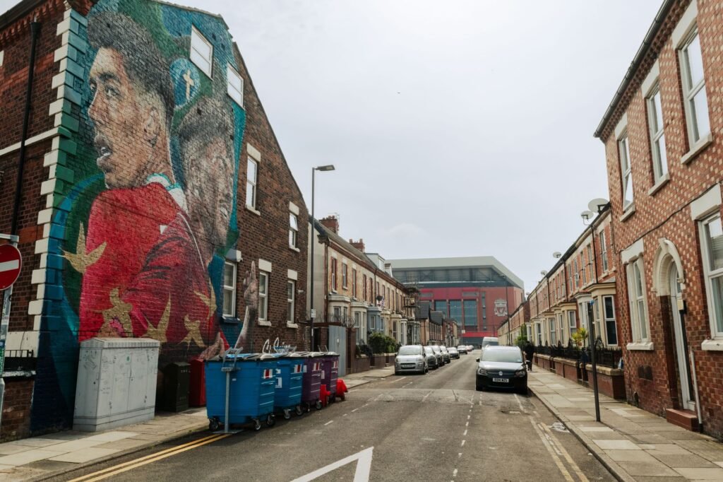 Street view in Liverpool with a vibrant mural and Anfield Stadium in the background.