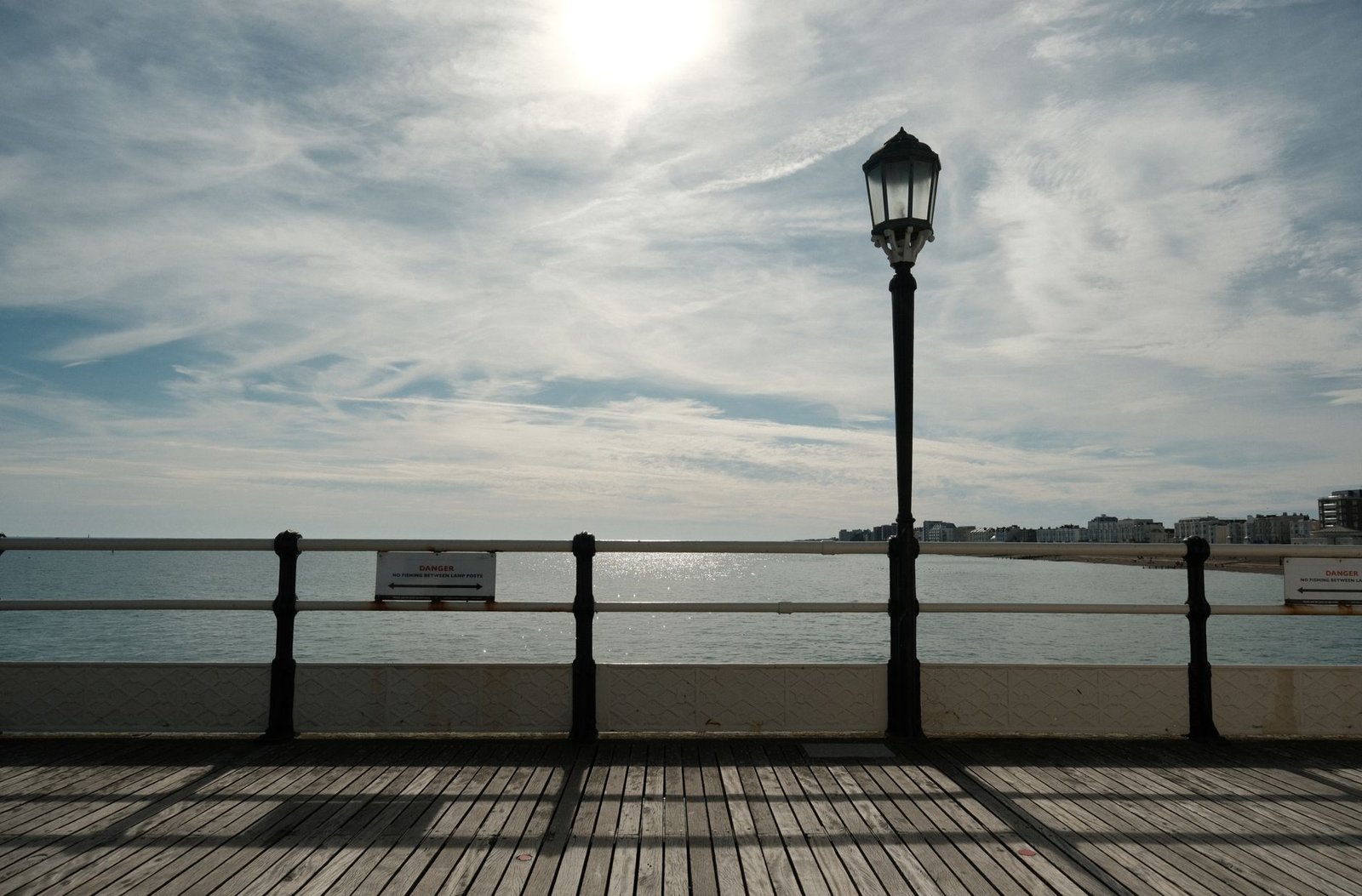Peaceful ocean view from a pier with a street lamp under a sunny sky.