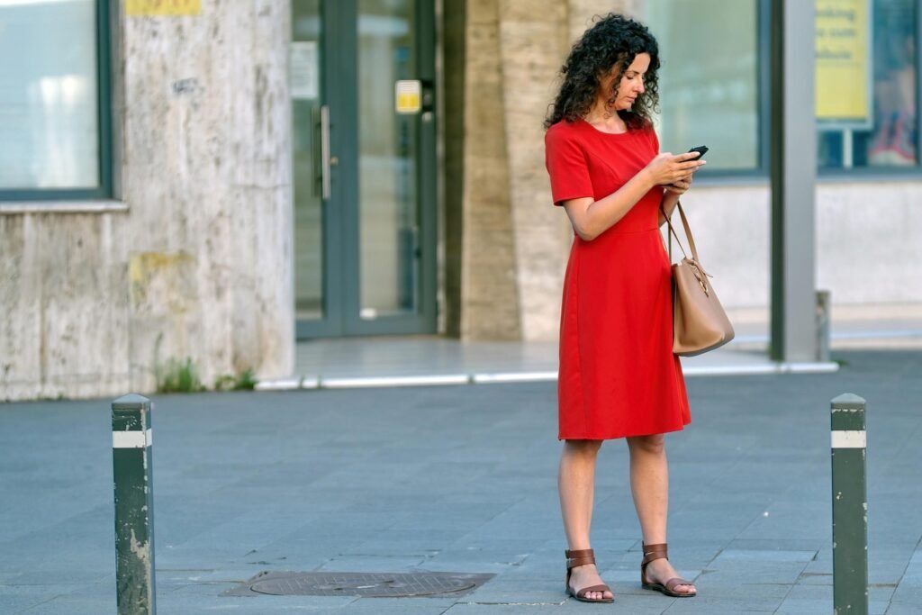 woman, red dress, phone, purse, bag, young, building, urban, town, person, sidewalk, snapshot, street photography, looking, s