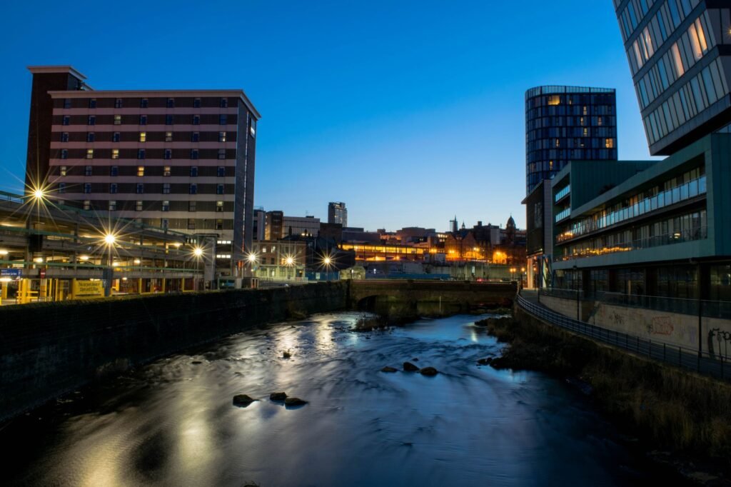 Cityscape at dusk featuring modern buildings and river reflections.