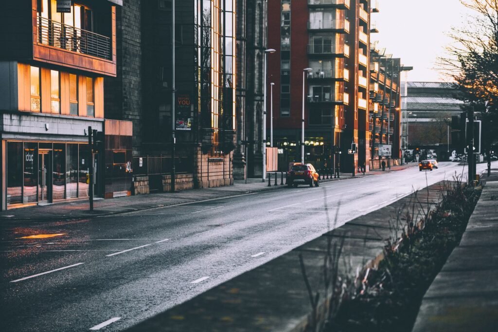 A city street with wet roads and illuminated buildings during evening, capturing an urban ambiance.