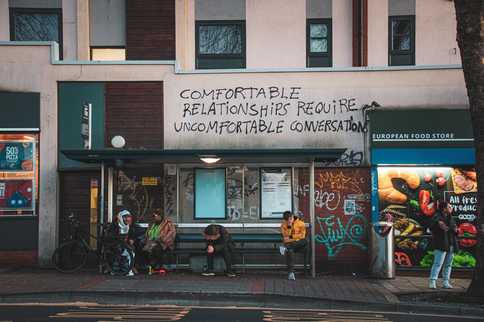 City street in Bristol with people waiting at a bus stop below graffiti.