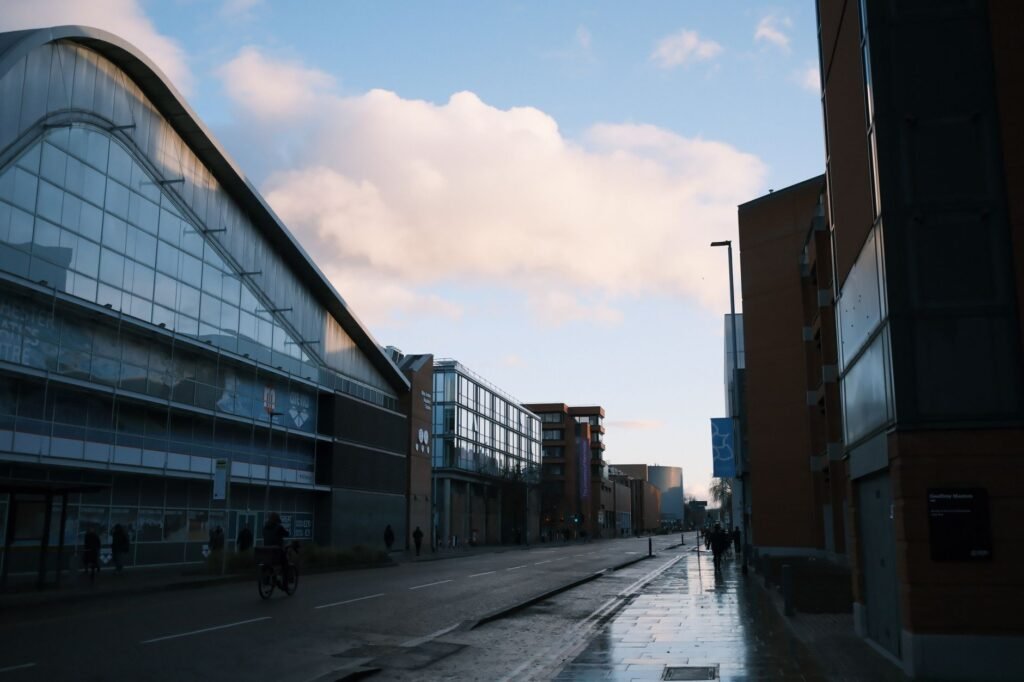 Quiet city street at sunset with reflections on wet pavement and modern architecture.