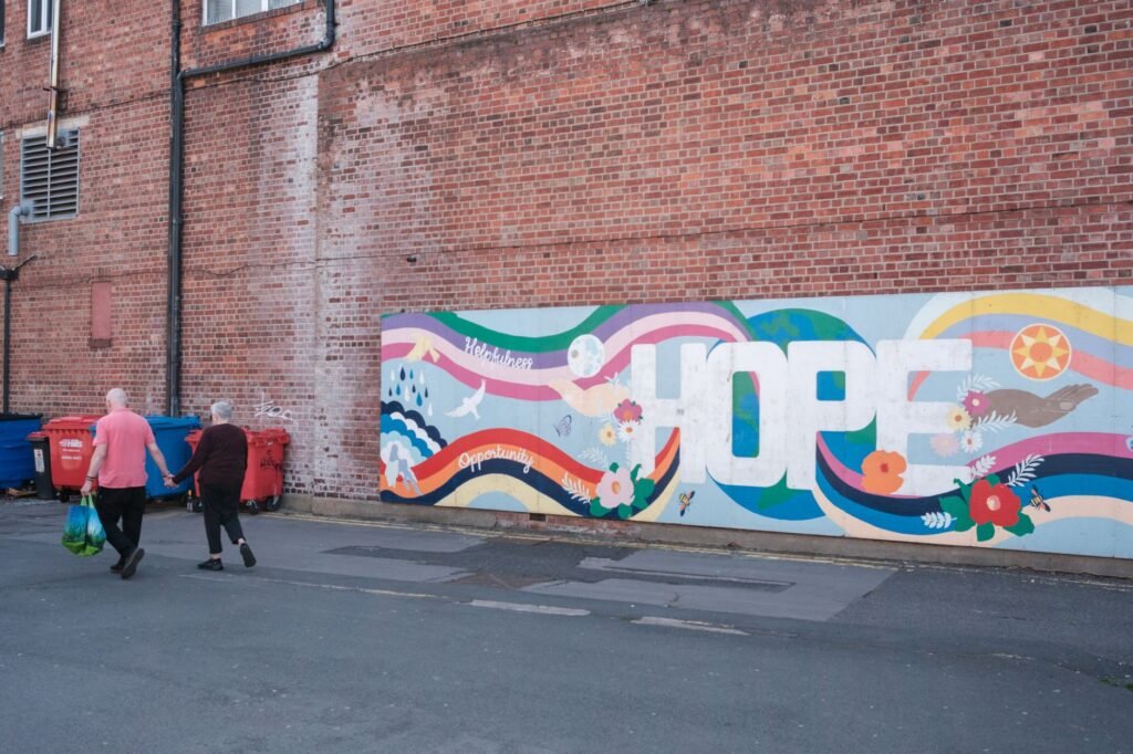 A couple walks by a colorful mural with the word 'Hope' on a brick wall.